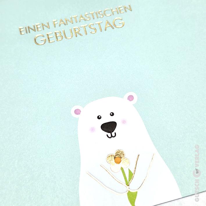 Eine hellblaue Grußkarte mit einem süßen weißen Eisbären, der eine kleine Goldfolienblume mit deutschem Text darüber hält.