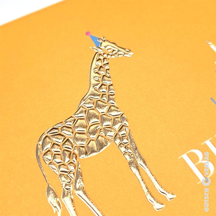 Eine glänzende goldgeprägte Giraffe mit einem kleinen blauen Partyhut auf einem strukturierten orangefarbenen Hintergrund mit teilweise sichtbarem Text.