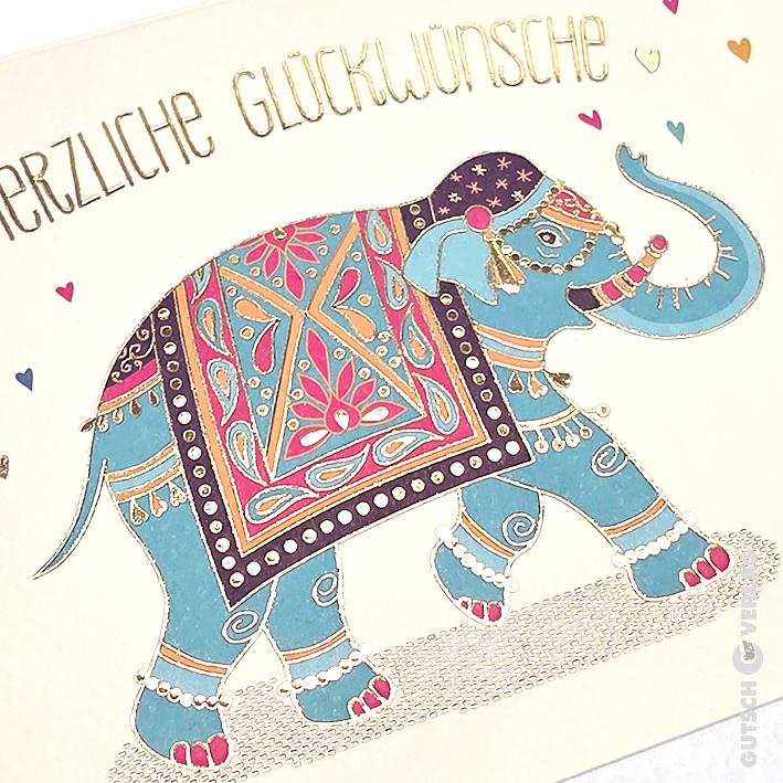 Eine dekorative Grußkarte mit einem blaugrünen Elefanten mit goldumrandeten Mustern und kleinen bunten Herzillustrationen.