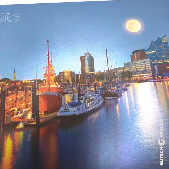 Ein malerischer Blick auf einen Hafen in der Abenddämmerung mit Booten, Stadtlichtern und einem Vollmond, der die Skyline beleuchtet.