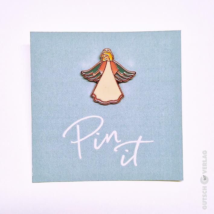 Eine dekorative Engelsnadel auf einer hellblauen Karte mit dem Text „Pin it“ in weißer Kursivschrift.