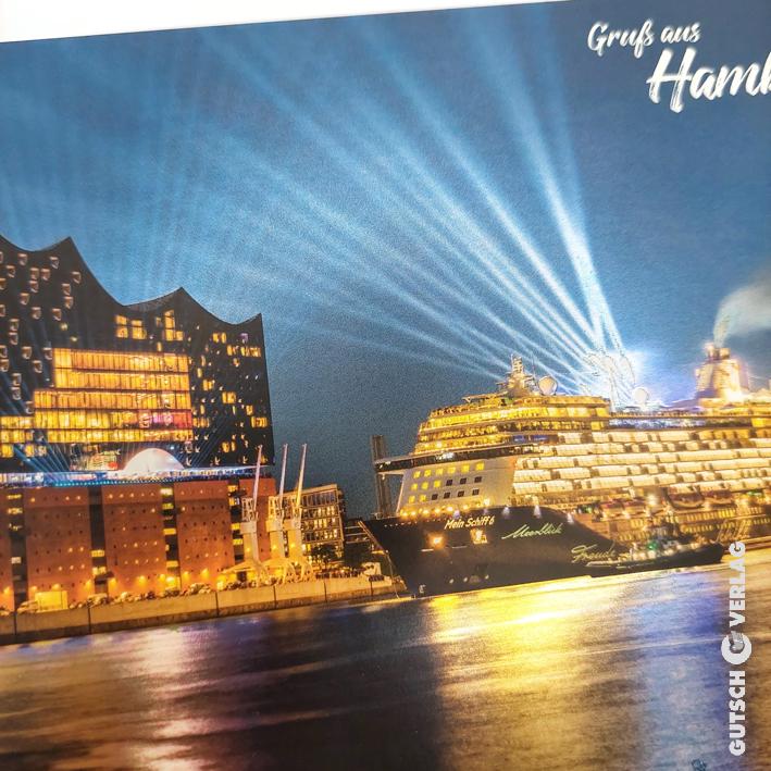 Beleuchtetes Kreuzfahrtschiff, das in Hamburg anlegt, mit moderner Architektur und lebendigen Lichtstrahlen bei Nacht.