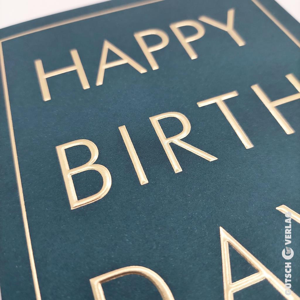 Eine Nahaufnahme einer dunkelgrünen Grußkarte mit den Worten „Happy Birthday“ in glänzender Goldfolienprägung.