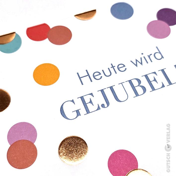 Eine weiße Karte mit dem Text „Heute wird GEJUBELT“, umgeben von buntem, metallischem und mattem kreisförmigem Papierkonfetti.