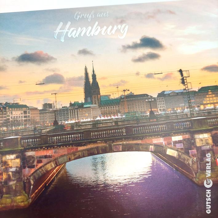 Malerischer Blick auf Hamburg bei Sonnenuntergang mit einer Brücke und historischen Gebäuden, die sich im Wasser spiegeln.