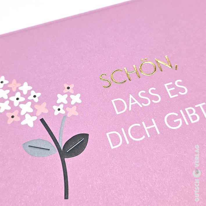 Eine Nahaufnahme einer hellvioletten Grußkarte mit einer stilisierten Blumenillustration und deutschem Text in Gold und Weiß.