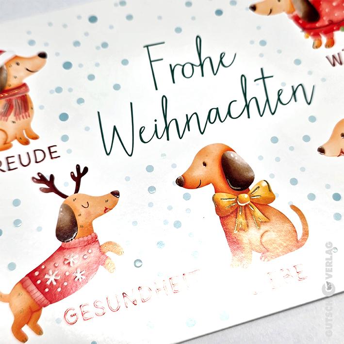 Eine Weihnachtskarte mit niedlichen illustrierten Dackeln in Pullovern und Rentiergeweihen inmitten blauer Schneepunkte.